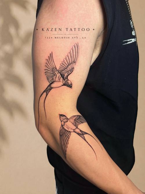 Two swallows in flight on the upper arm, fine line tattoo by Amina at KAZENTATTOO, Los Angeles