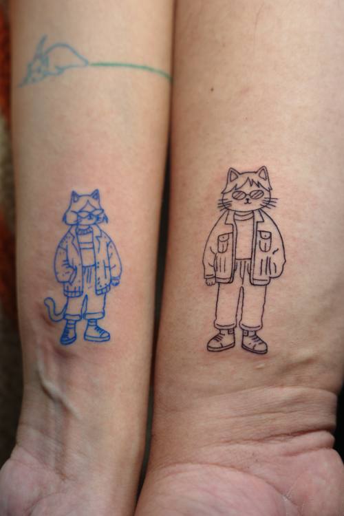 Matching cartoon figures on two forearms by Amina at KAZENTATTOO, Los Angeles