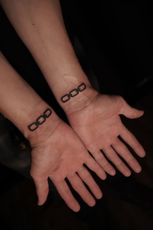 Matching chain bracelets on two wrists, fine line tattoos by Amina at KAZENTATTOO, Los Angeles