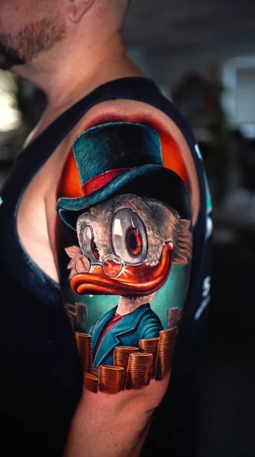 Cartoon duck in a top hat with coins, colour upper arm tattoo by Livio at KAZENTATTOO, Los Angeles