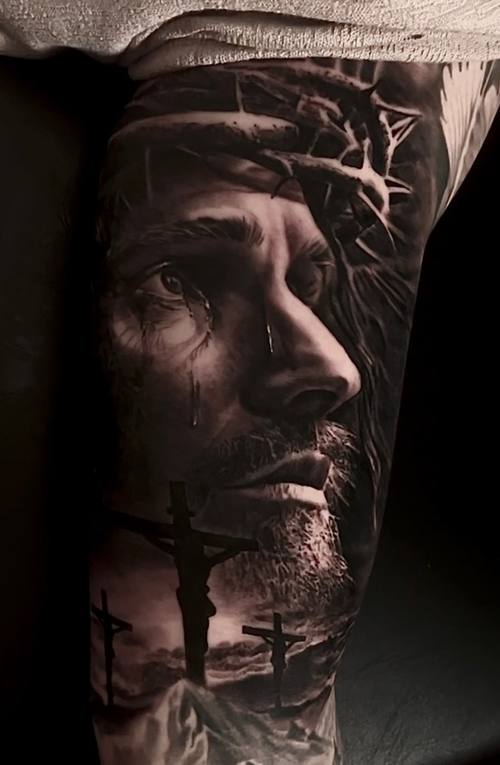 Jesus looking upward with three crosses on a hill, black and grey realism forearm tattoo by Marko at KAZENTATTOO, Los Angeles