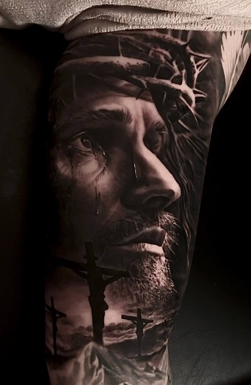 Jesus looking upward with three crosses on a hill, black and grey realism forearm tattoo by Marko at KAZENTATTOO, Los Angeles