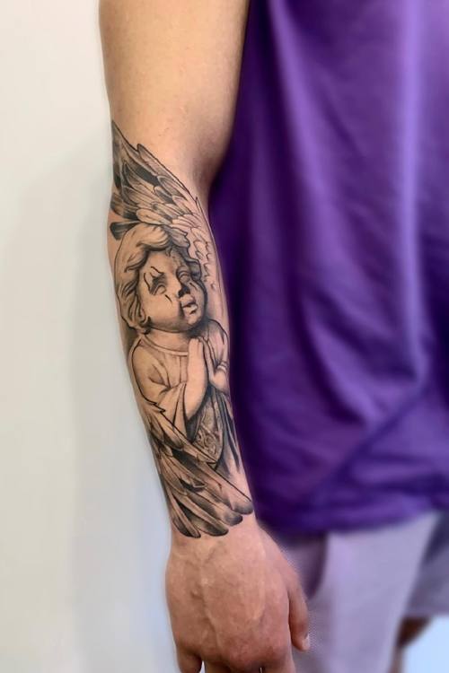 Black and grey cherub angel with wings and praying hands on the forearm by Padre at KAZENTATTOO, Los Angeles