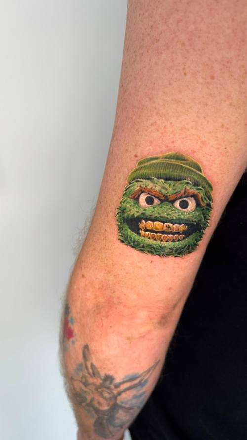 Color furry green monster with a knit cap and gold grin on the upper arm by Padre at KAZENTATTOO, Los Angeles