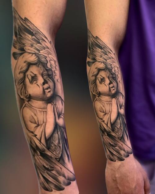 Black and grey cherub angel with wings and praying hands on the forearm by Padre at KAZENTATTOO, Los Angeles