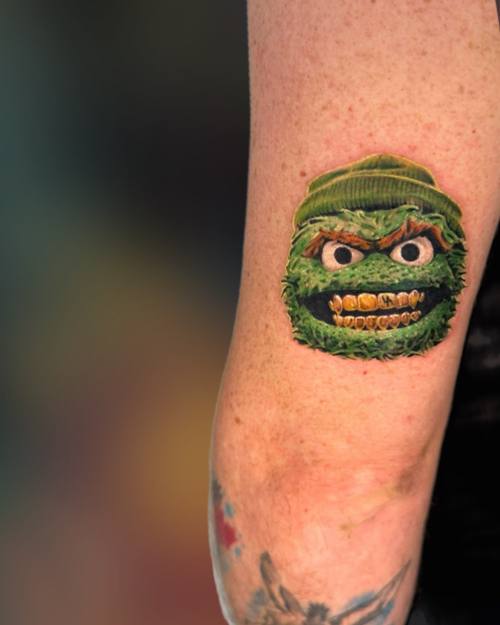 Color furry green monster with a knit cap and gold grin on the upper arm by Padre at KAZENTATTOO, Los Angeles