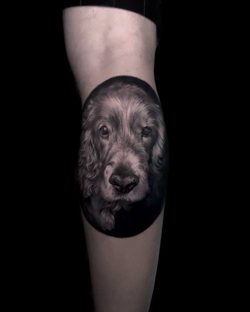 Dog portrait in a dark oval, black and grey calf tattoo by Vladimir Kozachenko